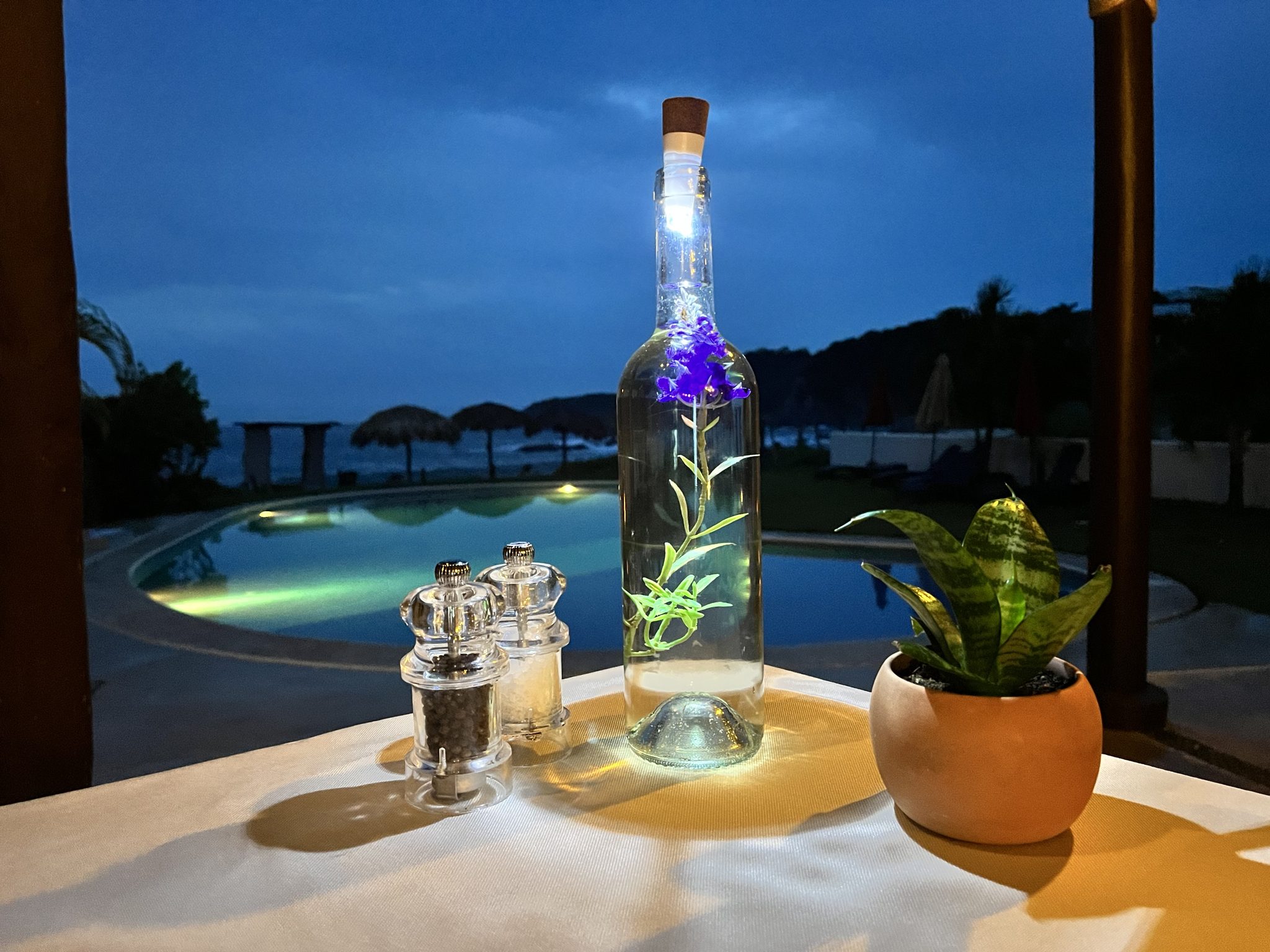 Une table dressée au crépuscule avec la piscine illuminée et la baie