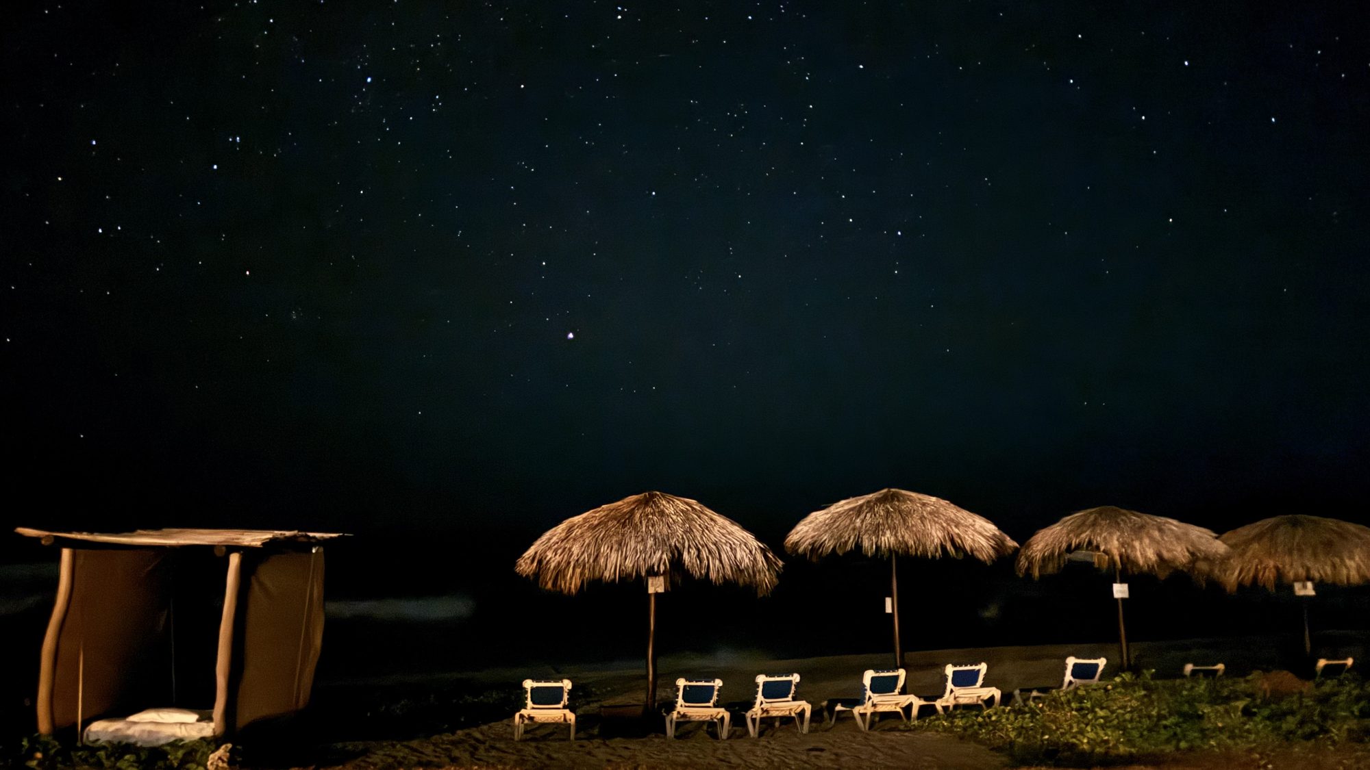 A starry night sky over the beach palapas at Salchi