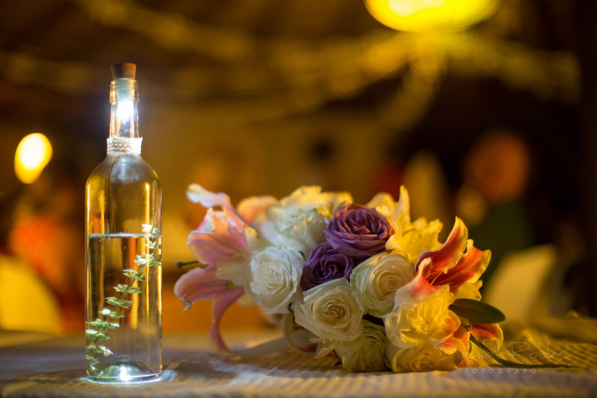 A bouquet of roses and lilies beside a bottle lamp