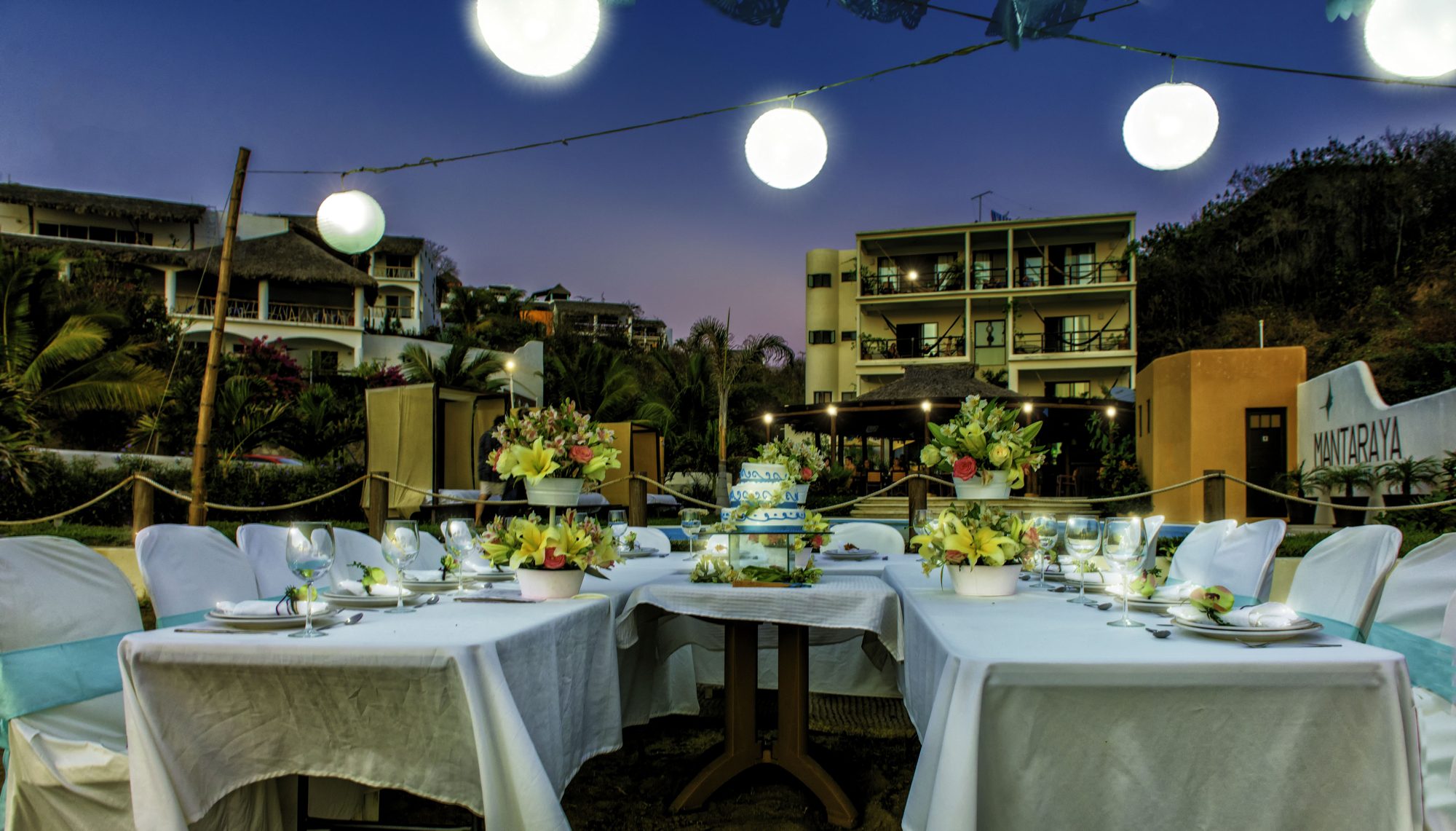 Long tables set under paper lanterns in front of the hotel