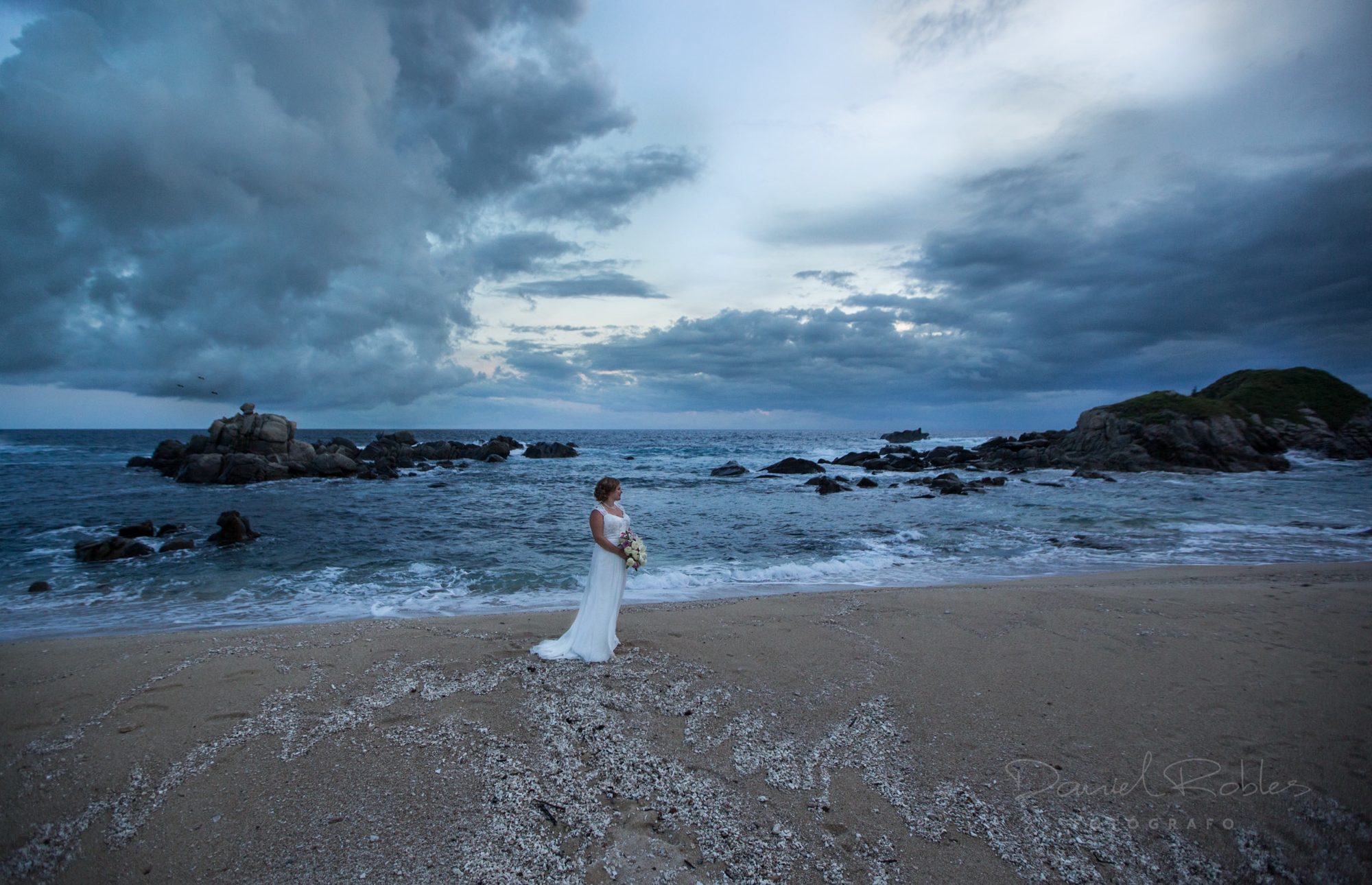 A bride alone on the beach under a dramatic sky