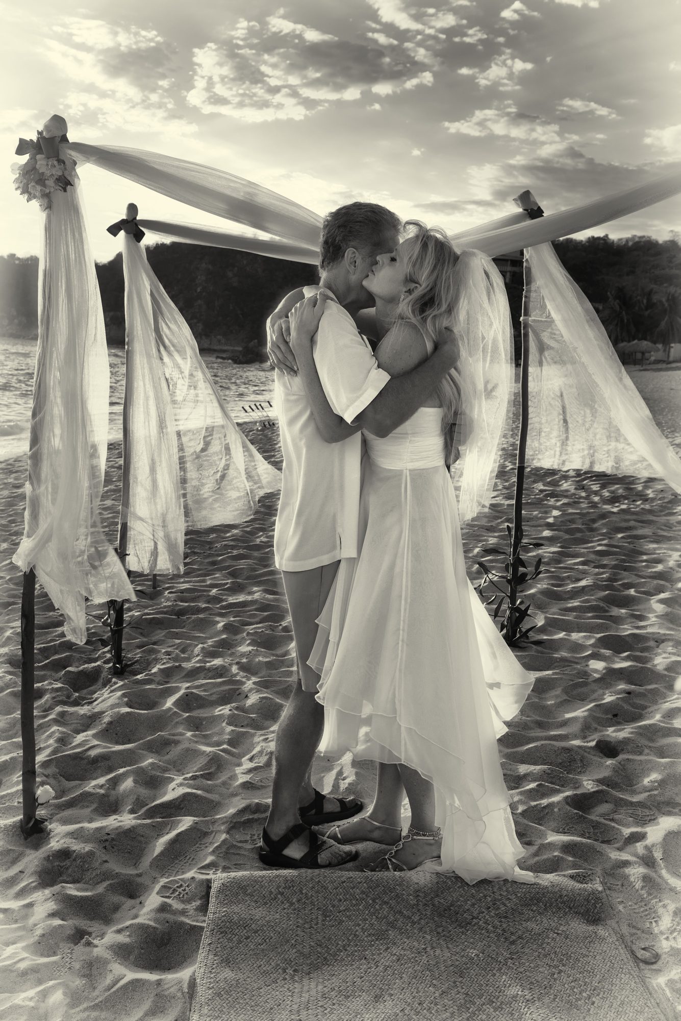 A couple kissing under a draped canopy on the sand