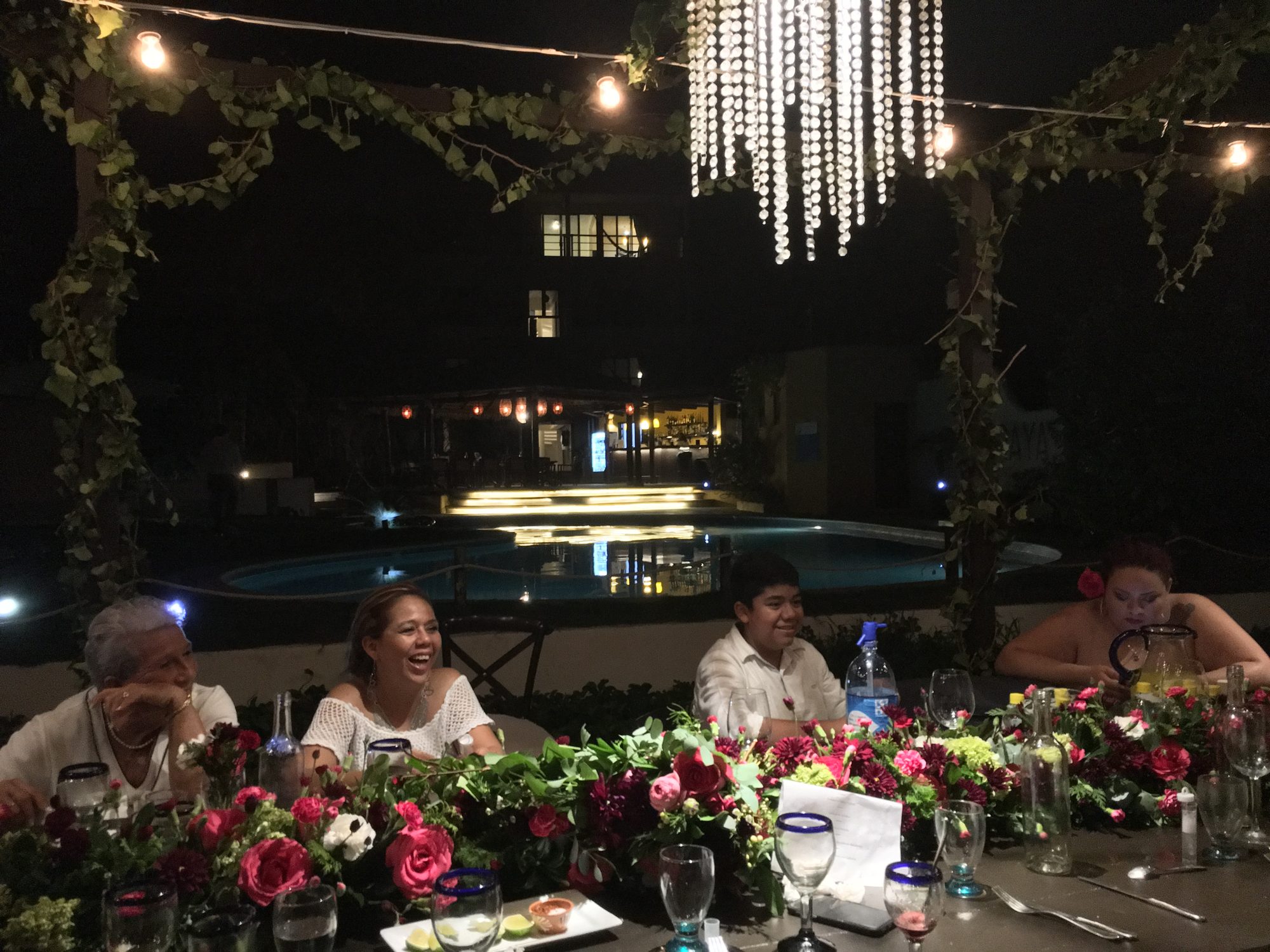 Guests at dinner by the pool under chandeliers