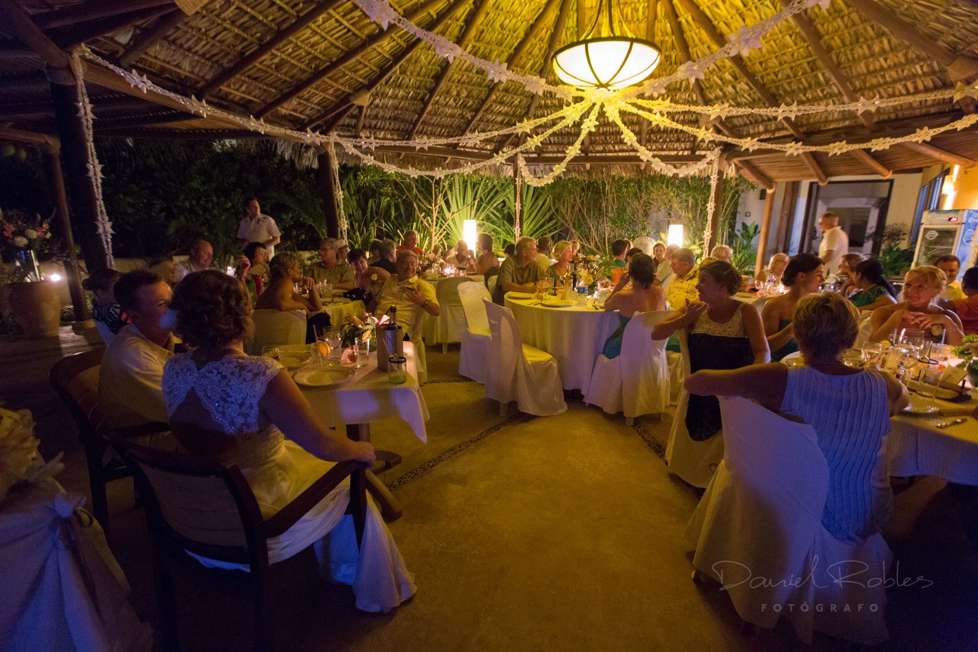 Wedding guests at dinner under the palapa, strung with garlands