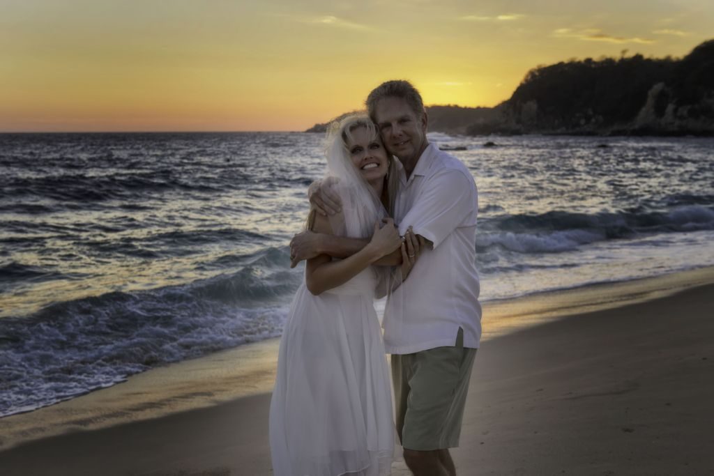 A newly married couple embracing on the beach at sunset