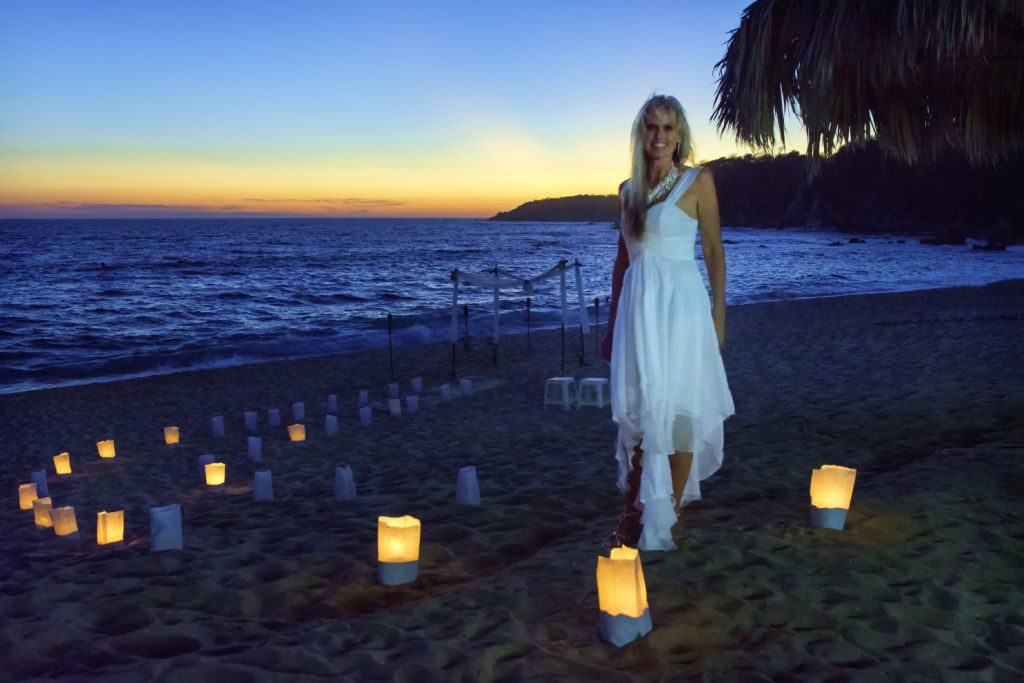 A bride in a white dress among candle lanterns on the beach at dusk